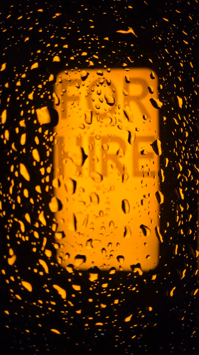 For Hire sign glowing through rain droplets